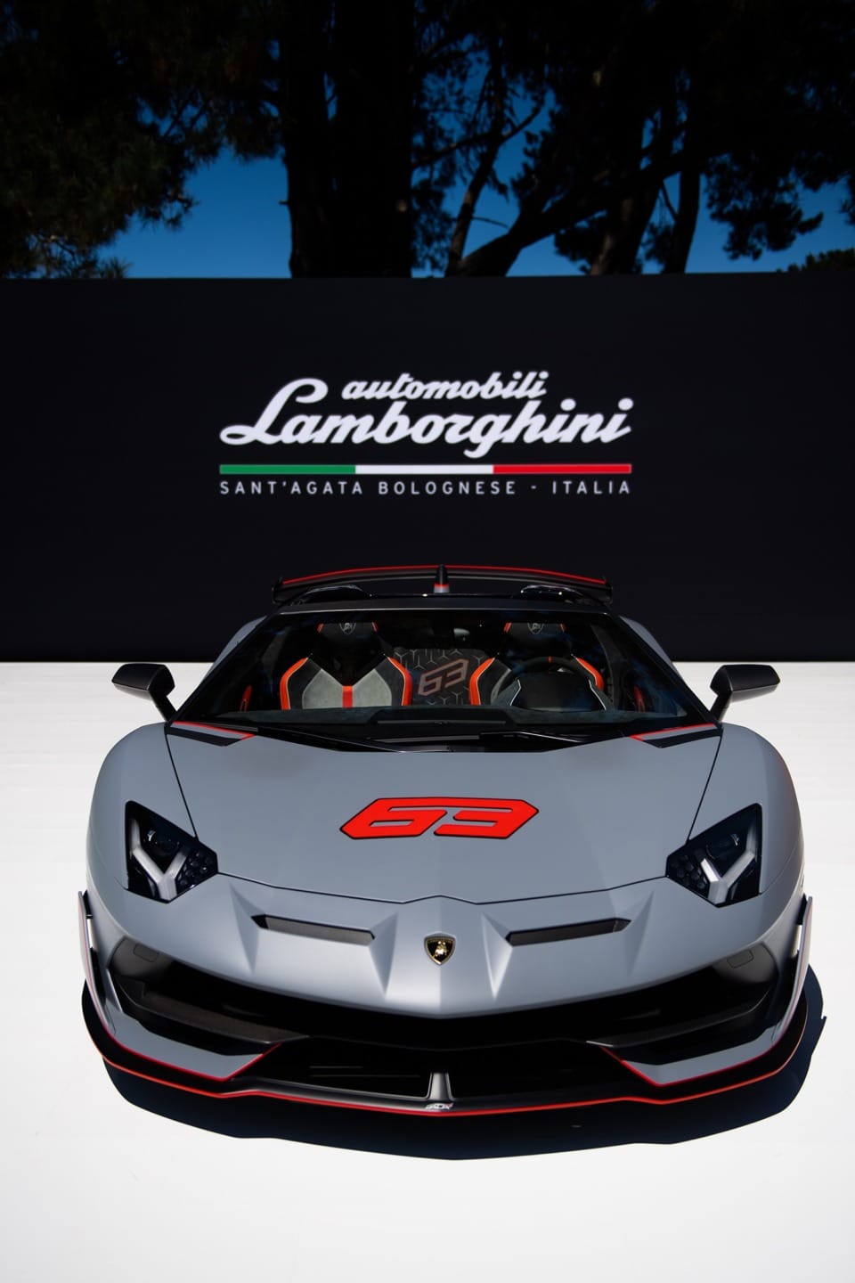 Front view of a gray Lamborghini sports car with red accents, displayed outdoors under a Lamborghini sign.