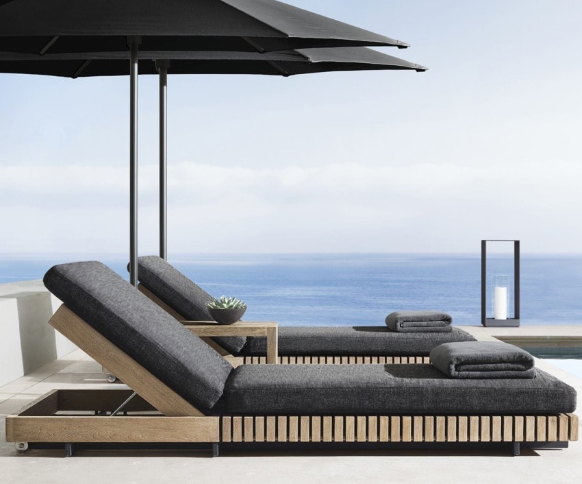 Poolside lounge chairs with dark cushions overlooking ocean under black umbrellas, small side table with succulent plant.