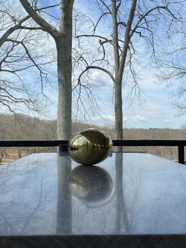 Golden orb on a reflective marble table with bare trees and a clear sky in the background
