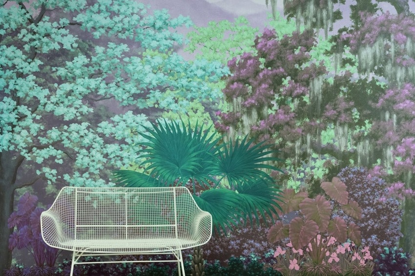 White metal bench in front of a colorful, lush garden mural featuring green, purple, and pink foliage.