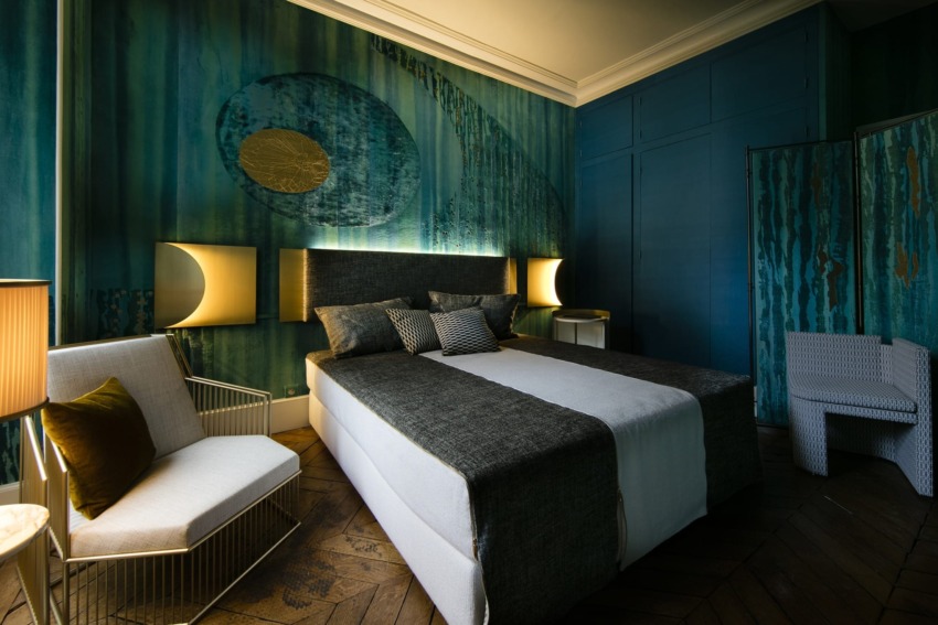 Luxurious bedroom with teal walls, modern lighting, a large bed, and stylish seating furniture.