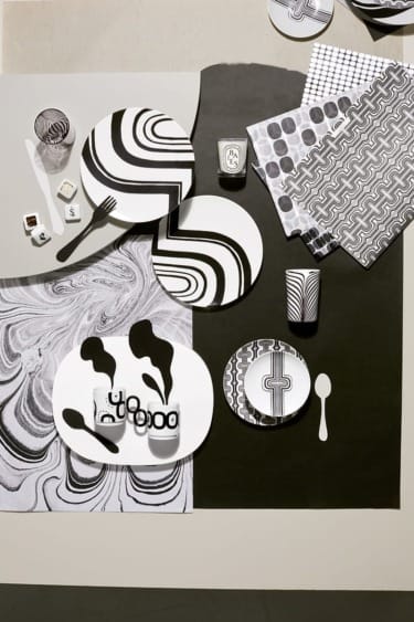 Monochrome abstract table setting with patterned plates, napkins, and cups on a bold black and white background.