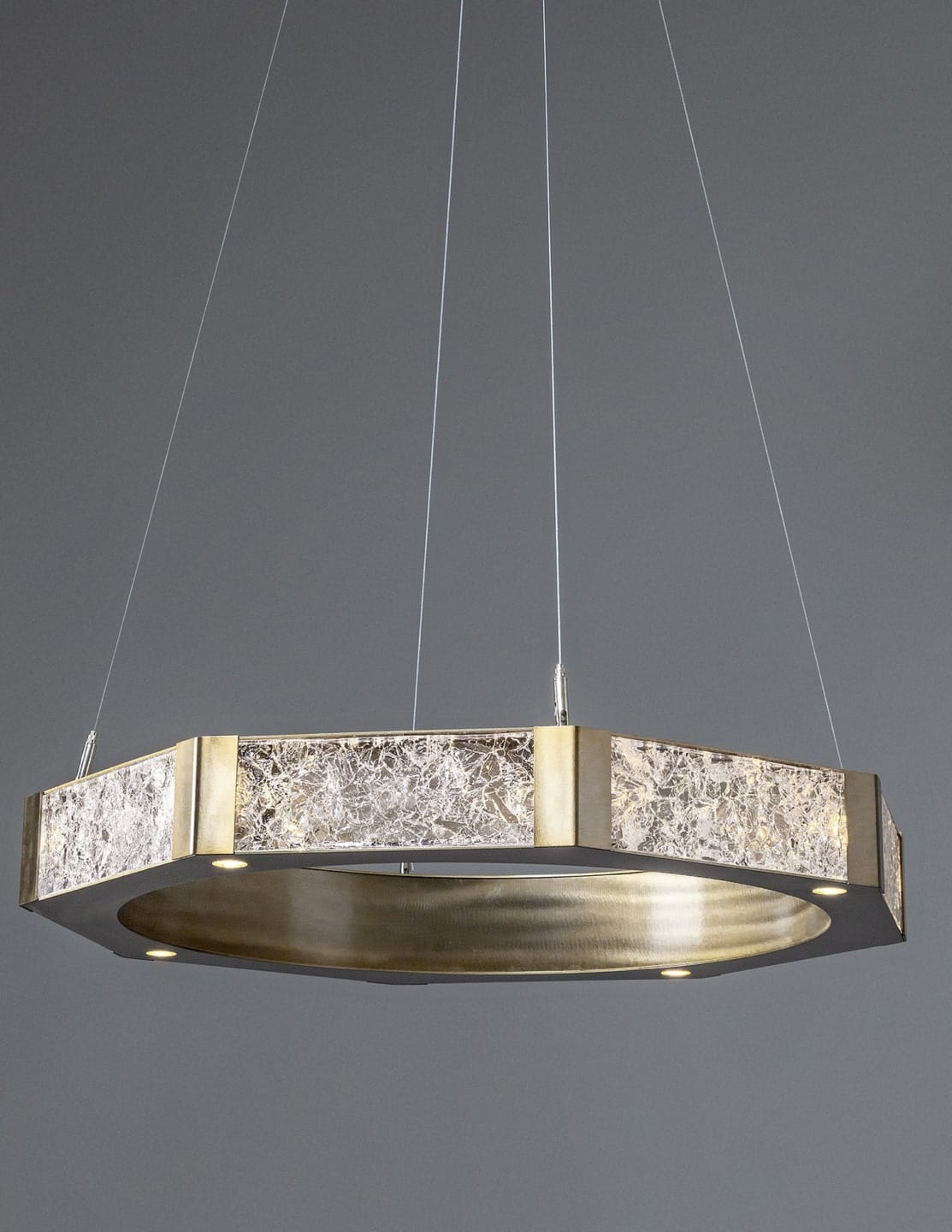 Modern circular chandelier with metallic finish and textured design, suspended from thin wires against a gray background.