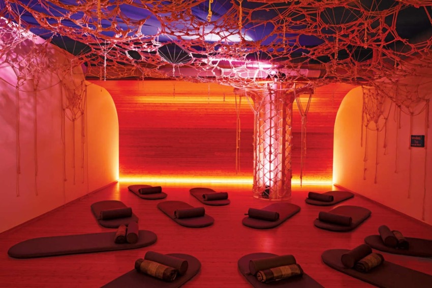 Yoga studio with woven ceiling art, red lighting, and mats arranged for meditation or relaxation.