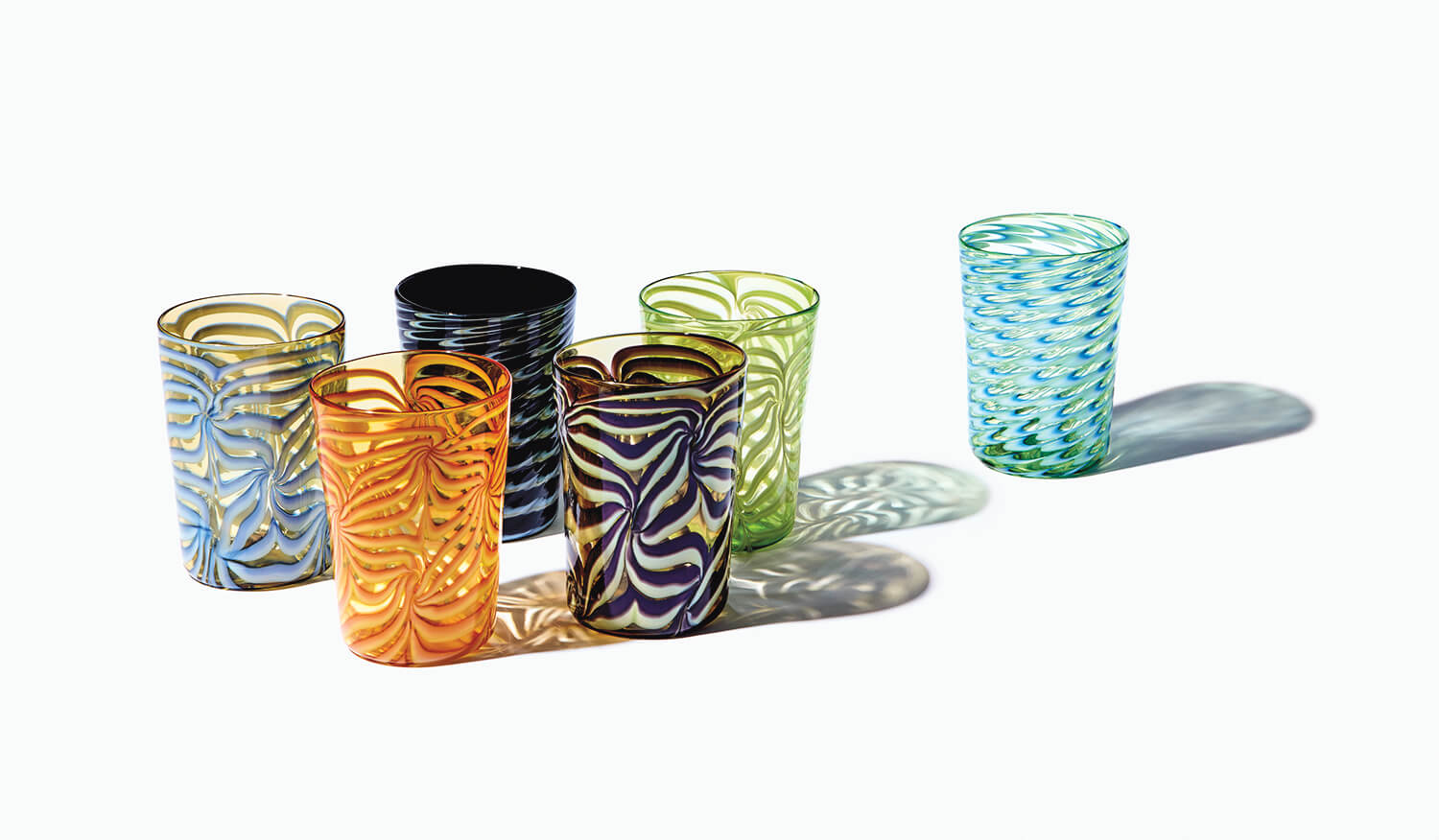Colorful, intricately patterned glass tumblers casting shadows on a light surface.