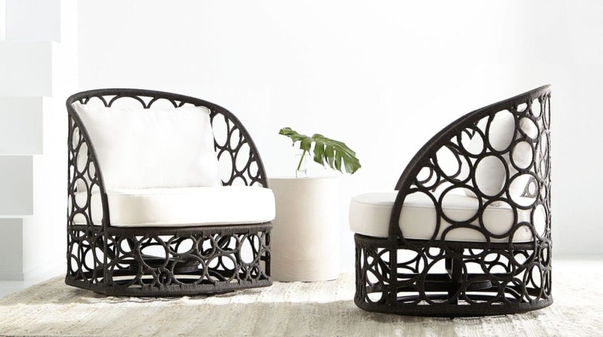 Two stylish wicker chairs with circular patterns and white cushions next to a small table holding a green plant.