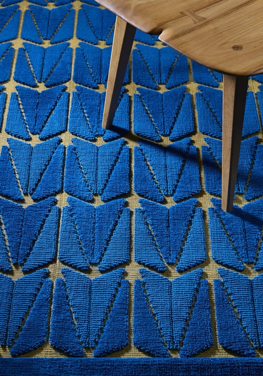 Blue geometric patterned rug with a wooden chair leg on top left corner.