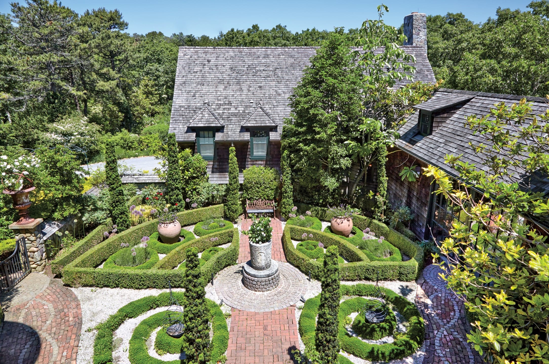 Aerial view of a cottage with a circular garden featuring intricate hedge patterns and a central fountain.
