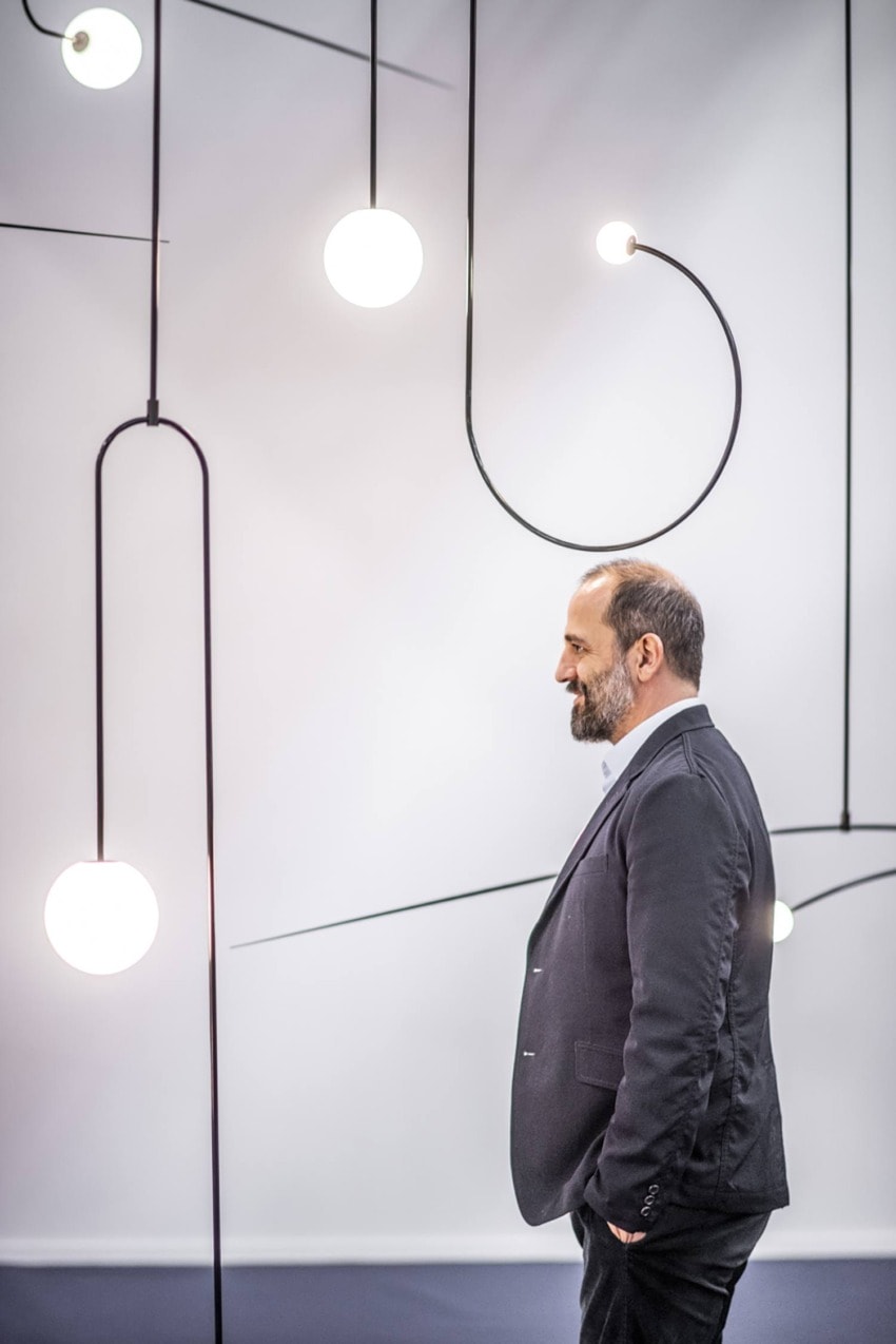 Man in a suit standing in a minimalist room with modern hanging lights.