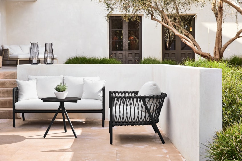 Outdoor patio with modern black and white furniture, including a loveseat, chair, small table, and potted plant.
