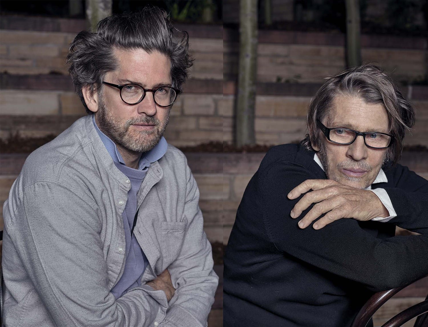 Two men wearing glasses sitting outdoors, one with arms crossed and the other leaning forward, both with casual expressions.