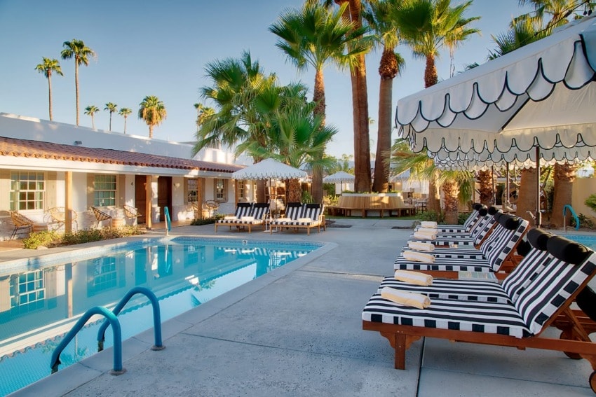 Palm tree-lined outdoor pool area with striped lounge chairs and umbrellas at a resort.