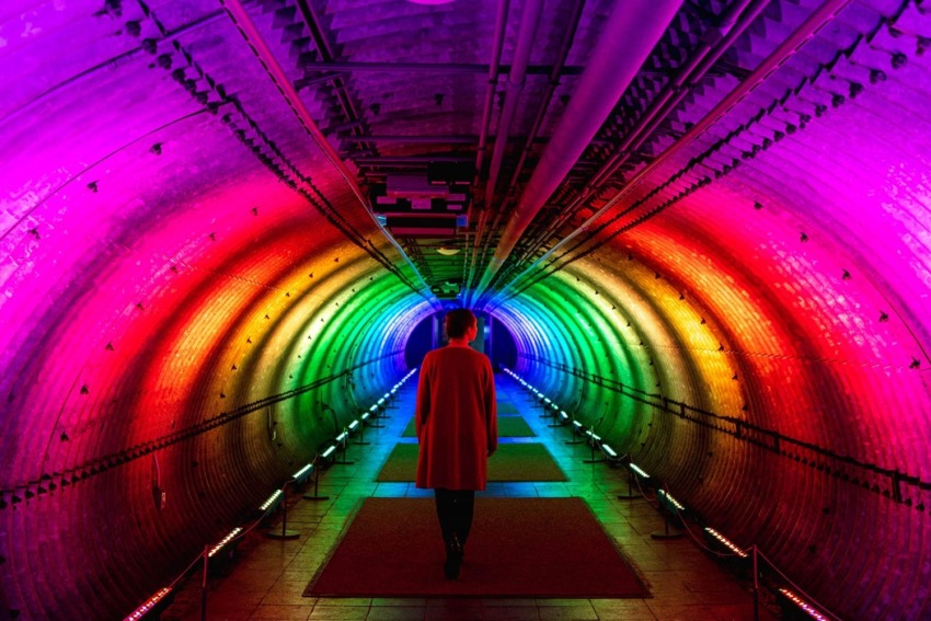 Person walking through a tunnel illuminated with vibrant rainbow colors, creating a vivid, futuristic atmosphere.