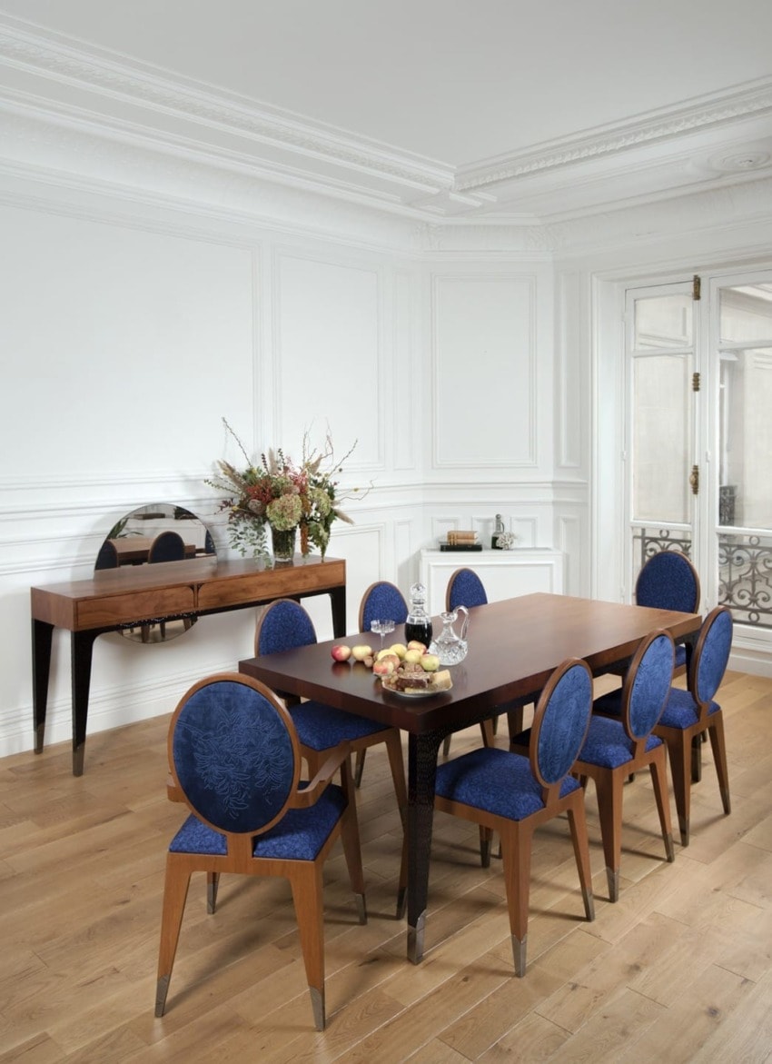 Elegant dining room with a wooden table, blue upholstered chairs, and a sideboard with a floral arrangement.