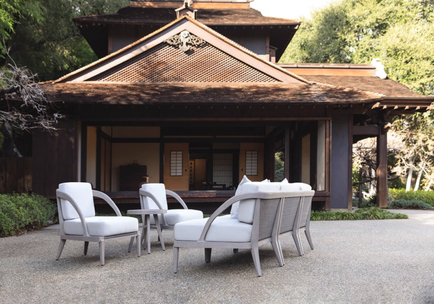 Outdoor patio furniture set with white cushions in front of a traditional building surrounded by greenery.