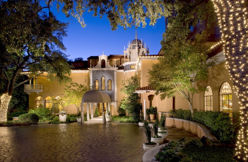 Elegant building exterior at dusk with warm lights, surrounded by trees and a cobblestone driveway.