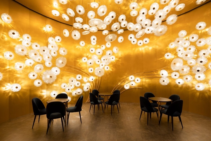 Illuminated cafe with round tables, black chairs, and a ceiling covered in unique circular light fixtures on a golden backdrop.