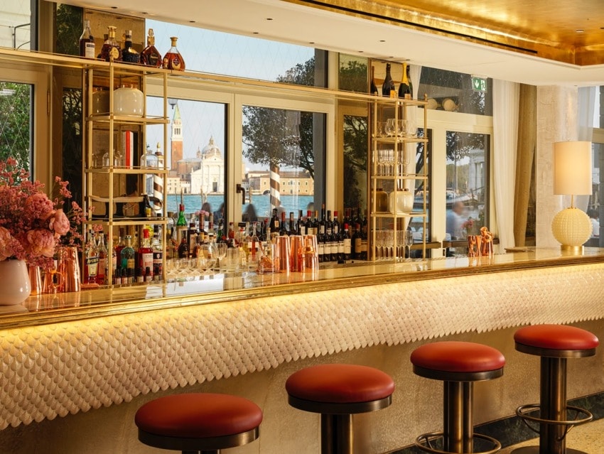 Luxurious bar with red stools, gold accents, and a well-stocked drink selection in a stylish, elegantly designed setting.