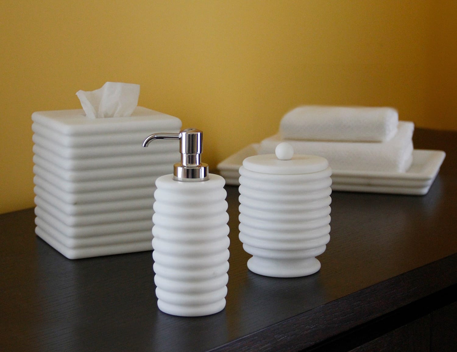 White bathroom accessories including a soap dispenser, tissue box, and towels on a dark countertop against a yellow wall.