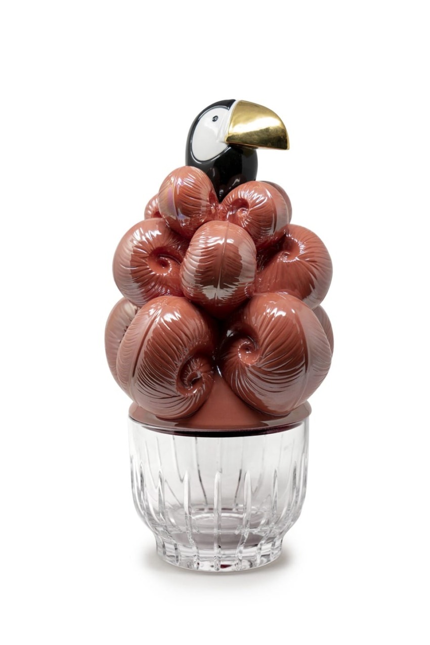 Glass sculpture of a toucan atop a cluster of brown, glossy curls on a clear, faceted base.