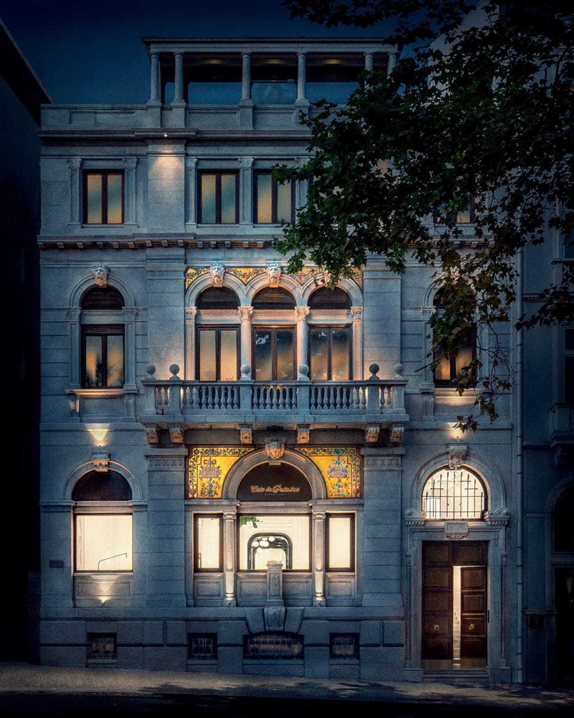 Illuminated historic building at night with ornate architecture and arched windows surrounded by trees.