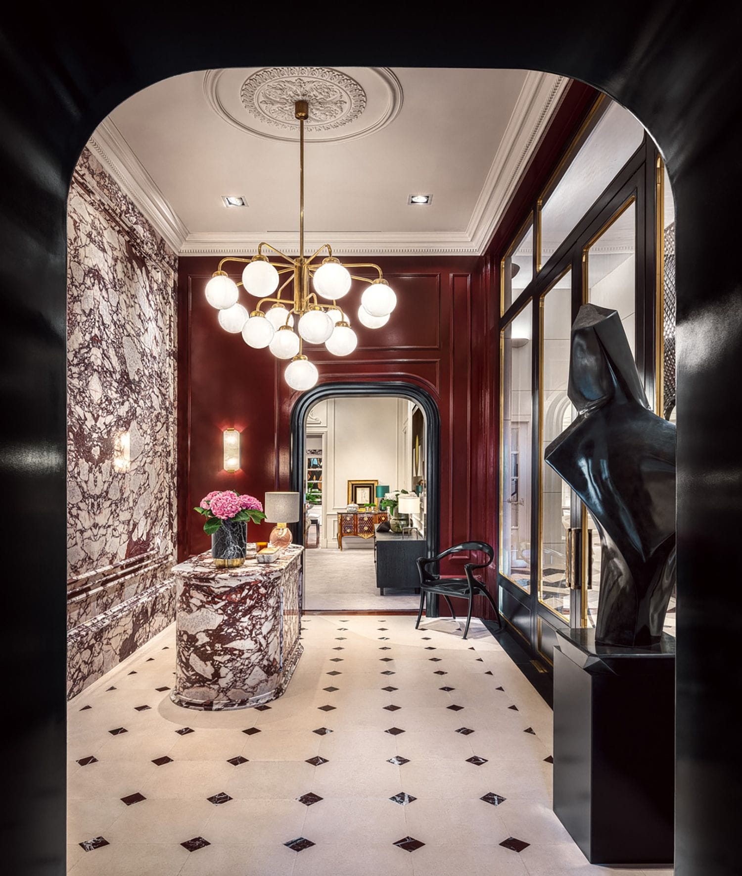 Elegant marble hallway with modern art sculpture, ornate chandelier, and arched doorway leading to a stylish interior room.