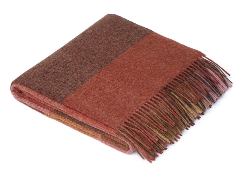 Folded wool blanket in shades of brown and red with fringed edges.