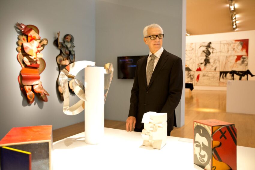 Person in a suit observing modern art sculptures and paintings in a gallery setting.