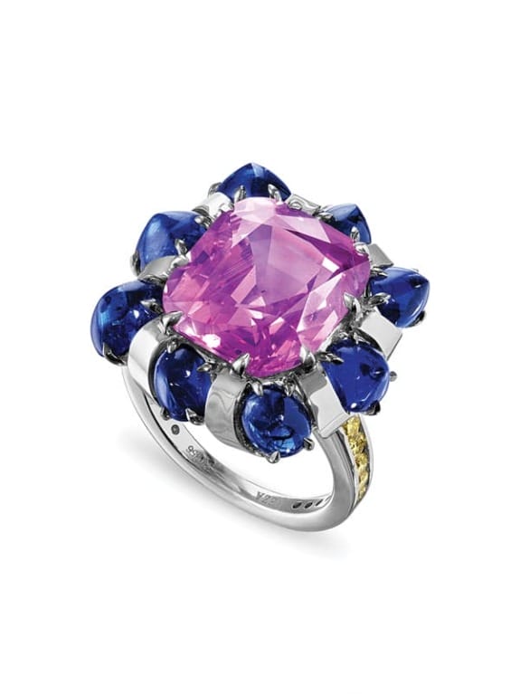 Silver ring with a large pink gemstone surrounded by blue gemstones in a floral design.