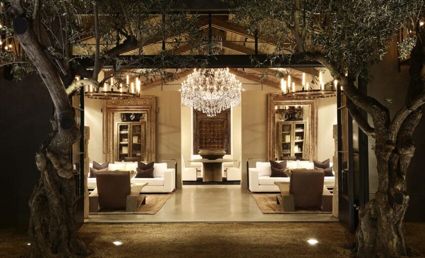 Luxurious living room with chandelier, rustic wood doors, and two sofas nestled between large indoor trees.
