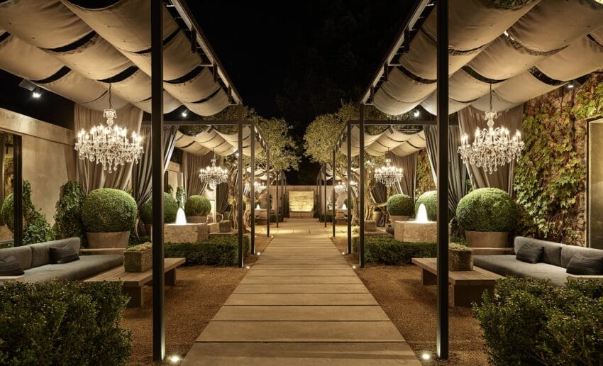 Elegant outdoor garden with chandeliers, fountains, and seating area under canopy at night.