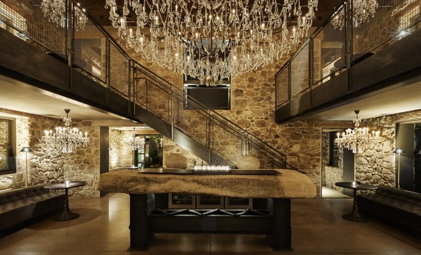 Luxurious stone-walled interior with spiral staircase, chandeliers, and modern furnishings.