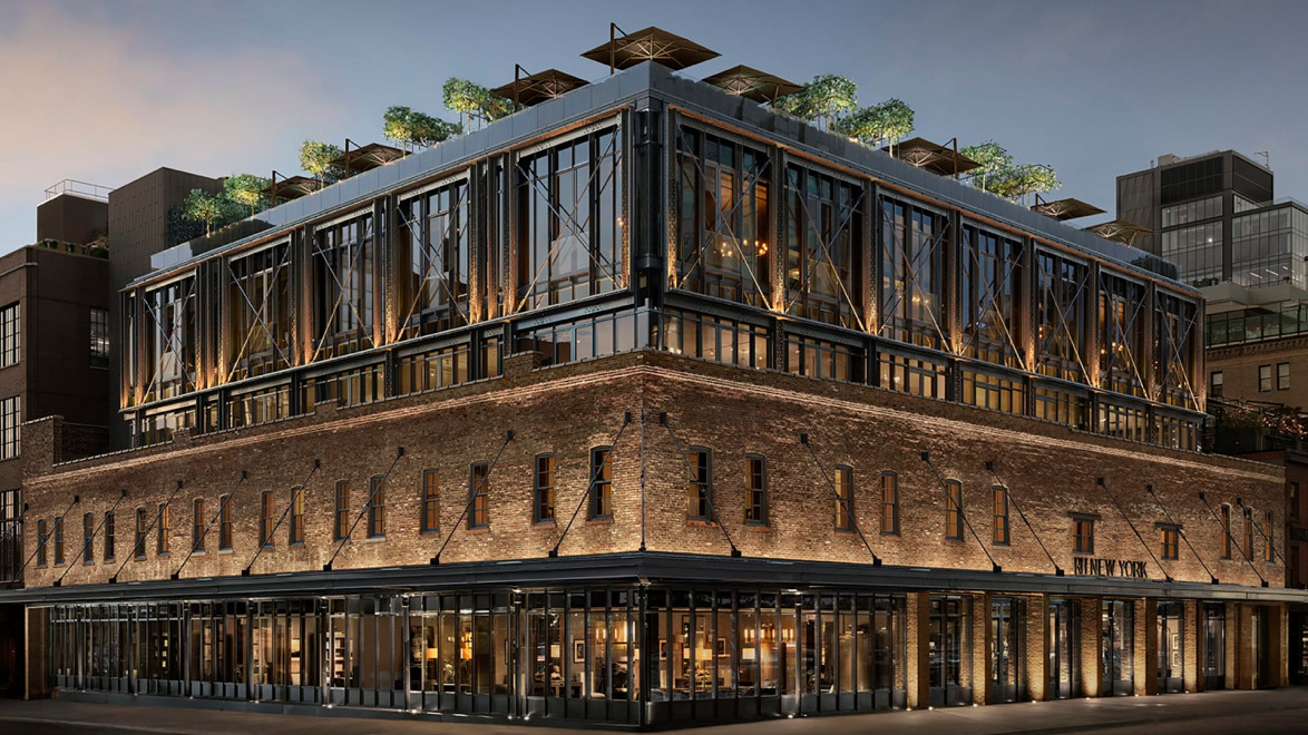 Modern multi-story brick building with large windows, rooftop garden, and evening lighting on a city street corner.