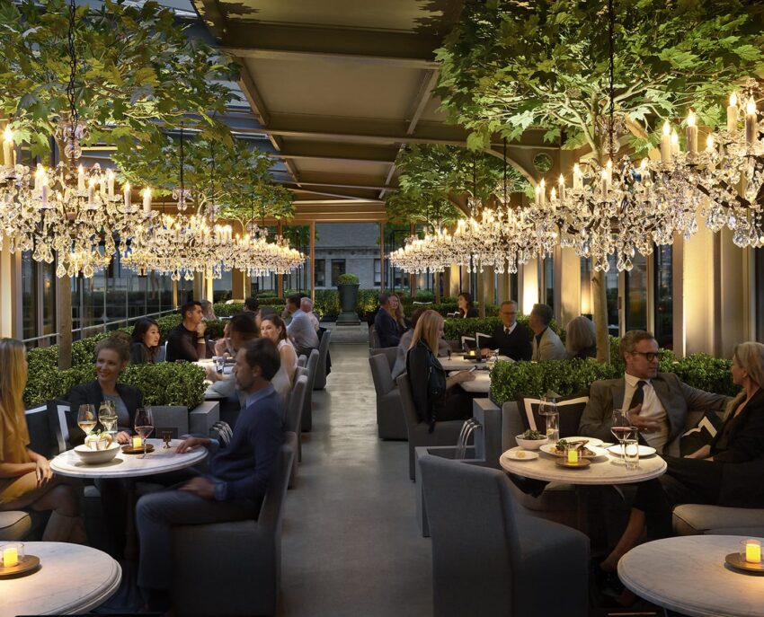 Indoor restaurant with diners, chandeliers, and plant decor, creating a cozy and elegant atmosphere at night.