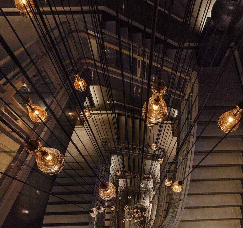 View from above of a spiral staircase with hanging pendant lights illuminating the scene.