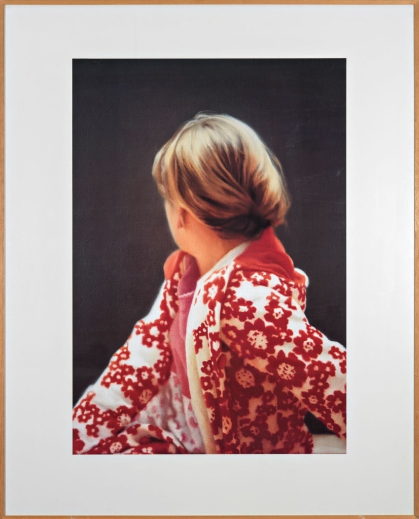 Child in a red and white floral jacket looking away against a dark background.