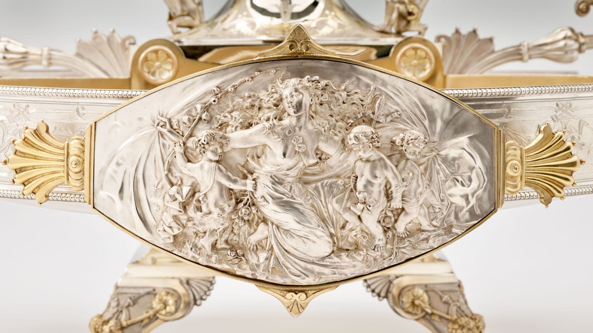 Intricately carved silver relief depicting a classical scene with mythological figures and ornate details.