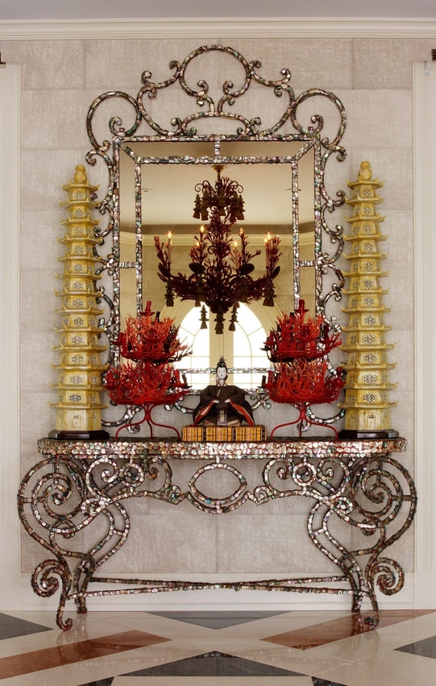 Elegant ornate mirror with decorative table featuring red and gold accents, flanked by two intricate pagoda sculptures.