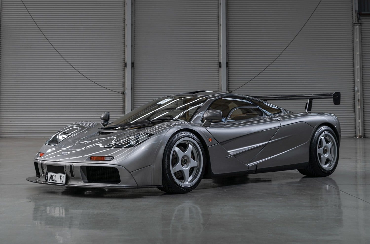 Sleek silver sports car parked in a large garage with smooth concrete floors and closed garage doors in the background.