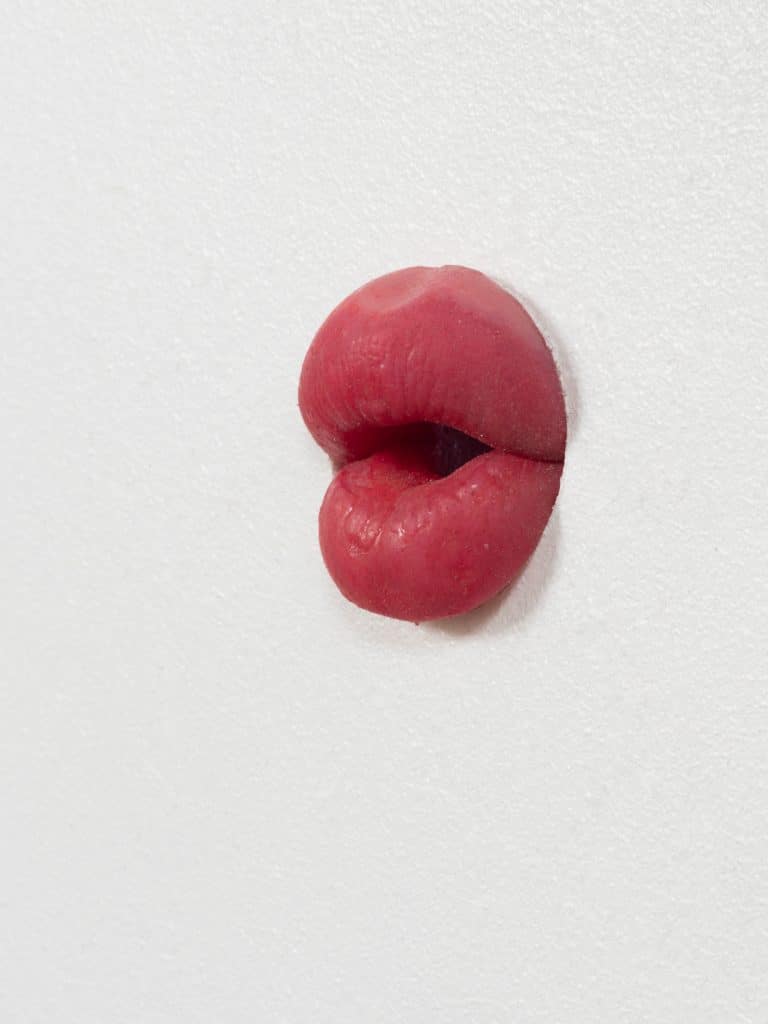 Red lips sculpture emerging from a white wall.