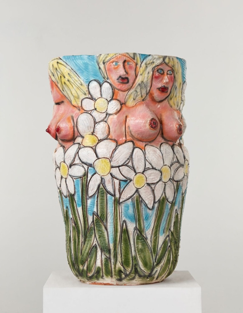 Colorful ceramic vase with floral and human figure motifs, featuring white flowers and abstract faces against a blue sky background.