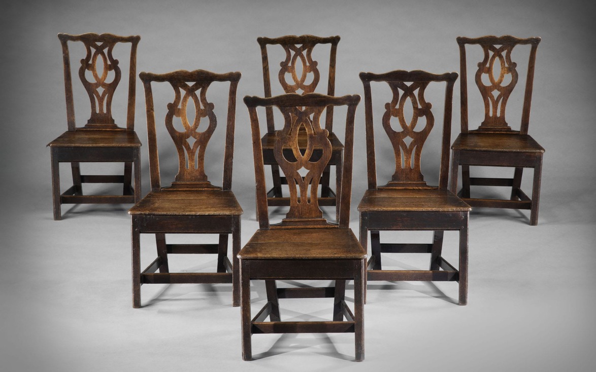 Six antique wooden chairs with ornate backrests arranged in two rows on a gray background.