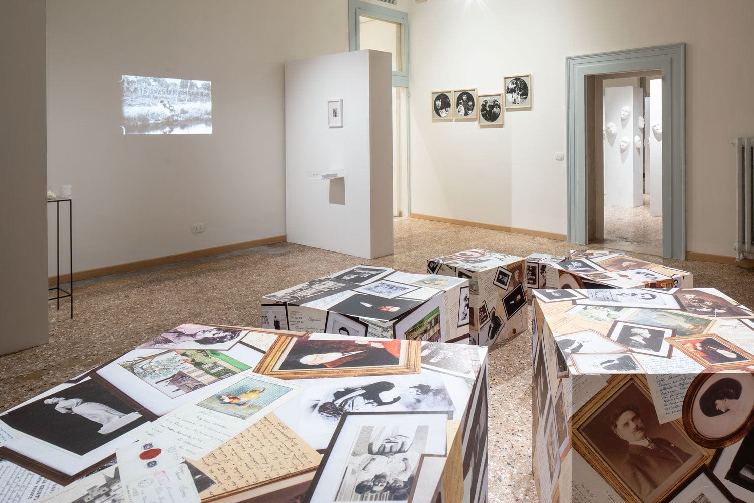 Art gallery exhibit with photographs and documents projected onto white cubes in a minimalist room.