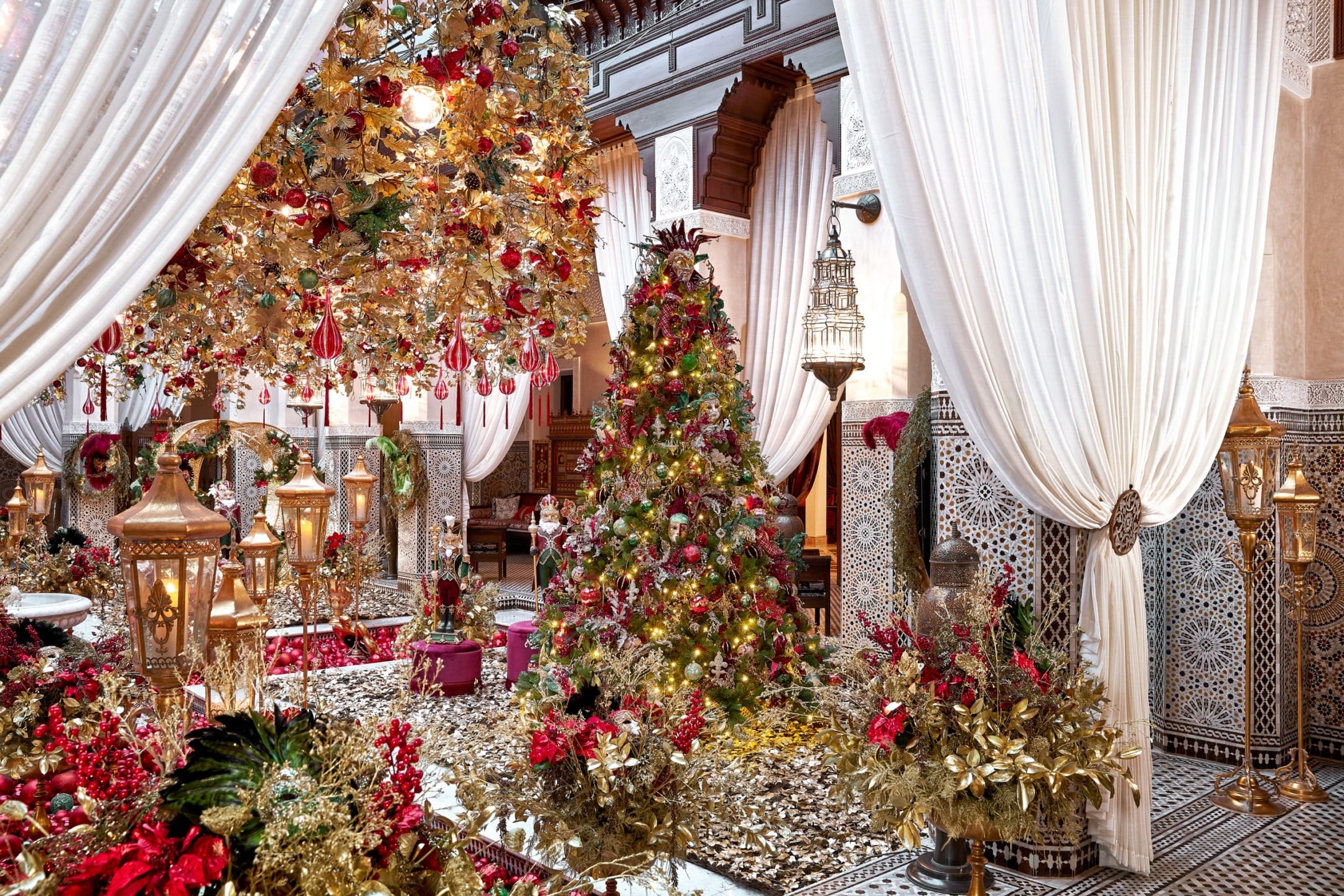 Lavishly decorated room with an ornate Christmas tree, red and gold floral arrangements, and intricate architectural details.