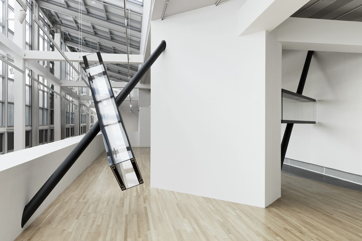 Modern art installation with slanted black beams and glass elements in a bright, spacious gallery with wooden flooring.