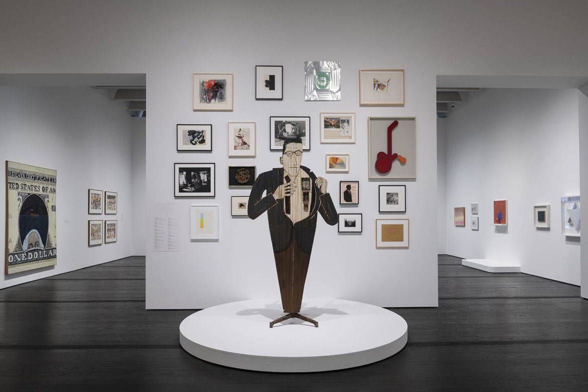 Art gallery interior with various framed artworks on white walls and a saxophone player sculpture on a central pedestal.