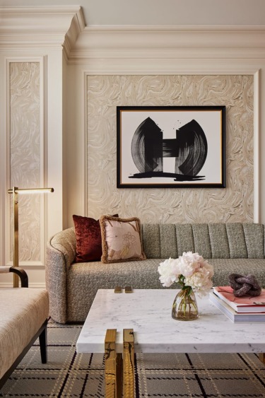 Elegant living room with patterned walls, abstract art, cozy sofa, stylish coffee table, and decorative pillows and flowers.