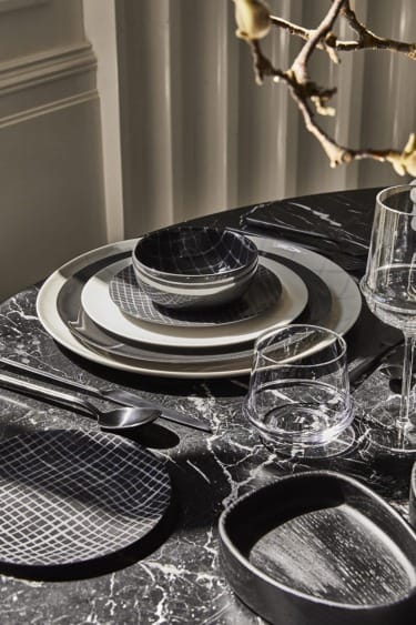 Black and white patterned dinnerware set arranged on a marble table with glasses and utensils.