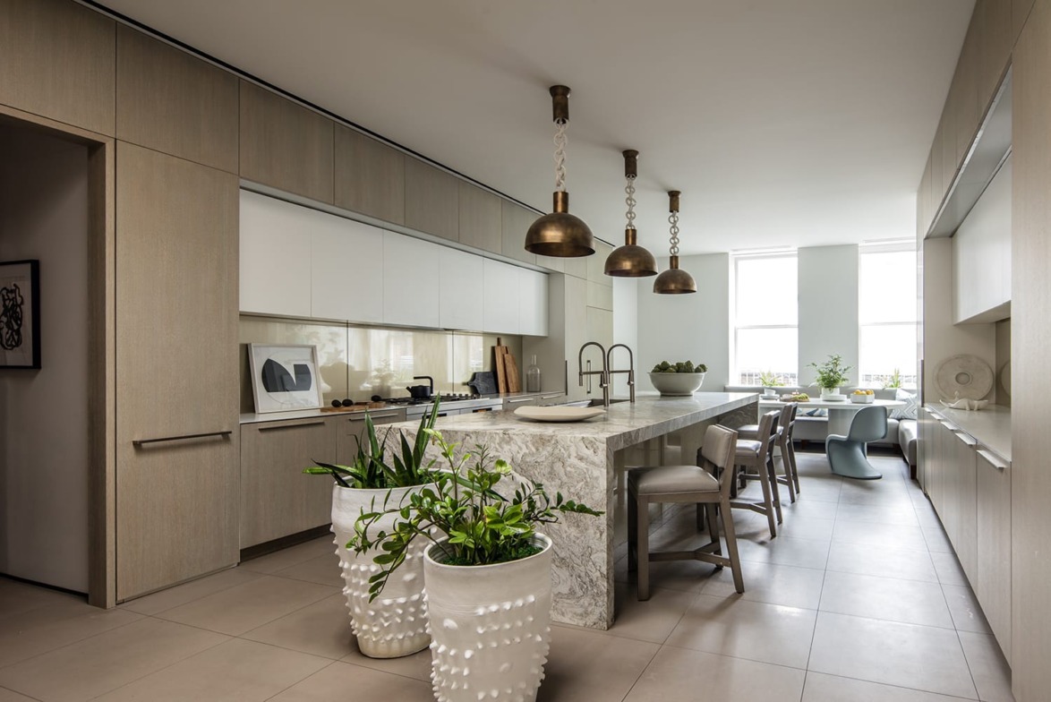 Modern kitchen with marble island, pendant lights, and potted plants, featuring sleek cabinetry and minimalistic decor.