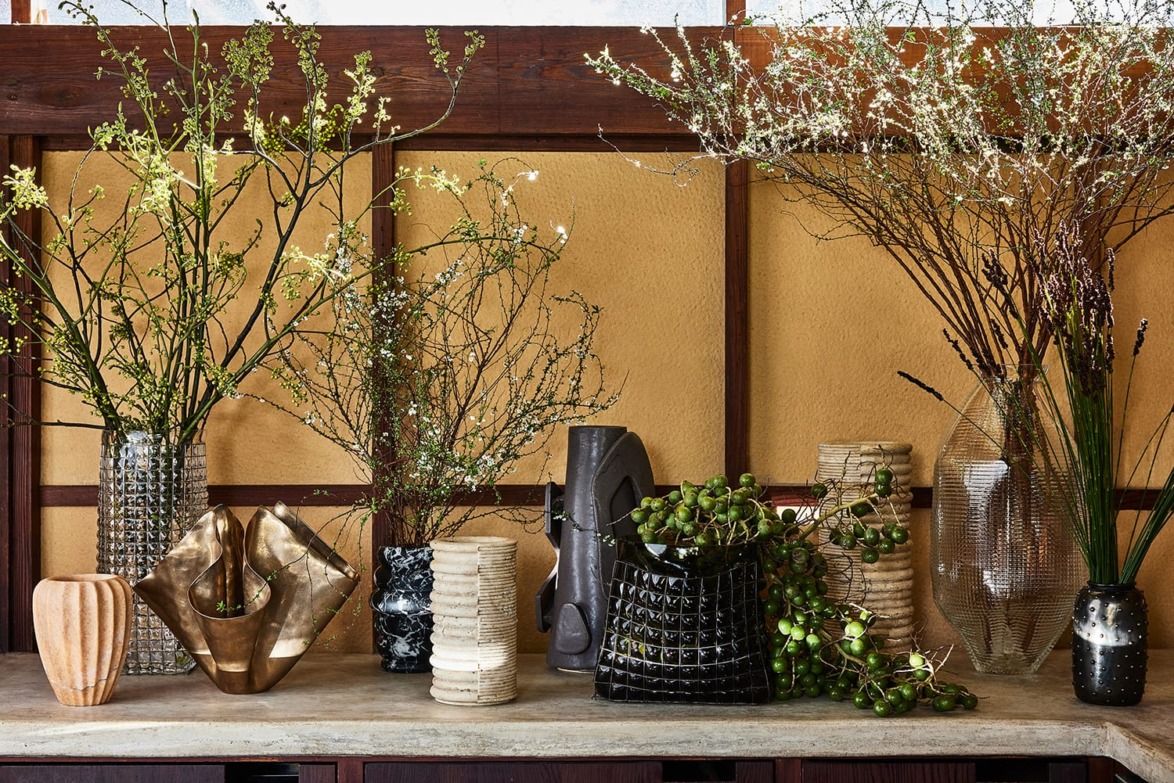 Assorted decorative vases and greenery on a shelf in a rustic setting